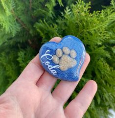 a hand holding a blue heart shaped rock with dog paw prints on it