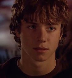 a close up of a person wearing a black shirt with curly hair and blue eyes