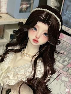 a close up of a doll with long hair wearing a dress and pearls on her head