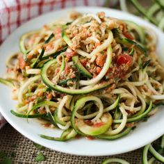 a white plate topped with zucchini noodles and meat covered in seasoning next to cucumbers