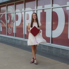 a girl in a white dress is holding a red book and posing for the camera