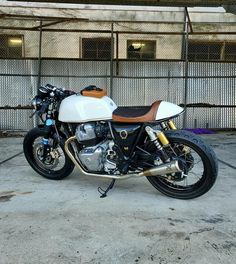 a white and brown motorcycle parked in front of a fenced off parking lot next to a building