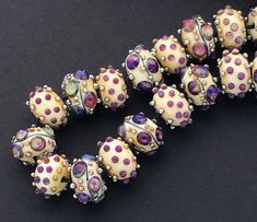 a bunch of beads that are sitting on a black surface with white and purple dots