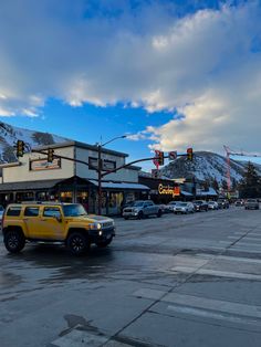 a yellow truck driving down a street next to a tall building and traffic lights with snow covered mountains in the background