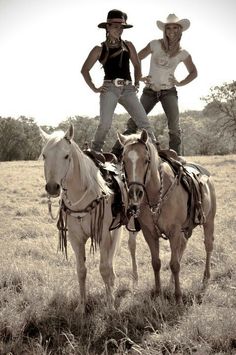 two women standing on top of horses in a field