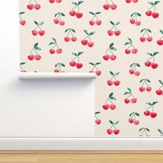 the wallpaper has cherries on it and is next to a white door with a wooden floor