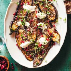 an eggplant dish with pomegranate and herbs on a white plate