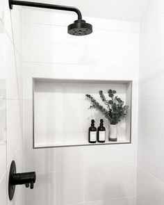 a white tiled bathroom with two bottles and a plant in the window sill on the wall