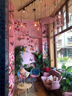 a living room with pink walls and lots of plants on the wall next to chairs