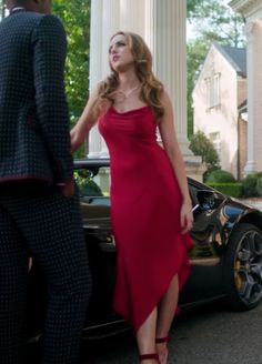 a woman in a red dress standing next to a car