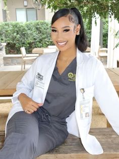 a woman sitting on top of a wooden bench wearing a white coat and grey pants