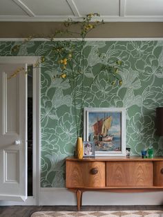 a living room with green wallpaper and a painting on the sideboard in front of it