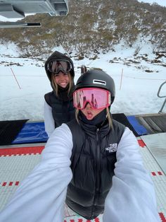 two people wearing skis and goggles taking a selfie in front of a chair lift