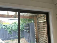 an open sliding glass door in front of a wooden fence and green plants on the wall