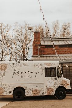 an ice cream truck parked in front of a brick building with trees and flowers on it