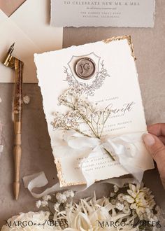 a person holding a wedding card in front of some flowers and writing on the paper