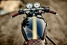 the handlebars and gauges of a motorcycle parked in a dirt road area