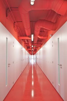 an empty hallway with red piping and white walls on both sides is lit by bright lights