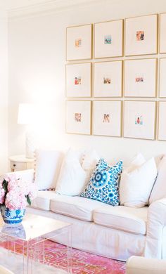 a living room filled with white furniture and lots of pictures on the wall above it