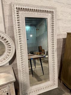 a large white mirror sitting on top of a wooden floor next to a dresser and table