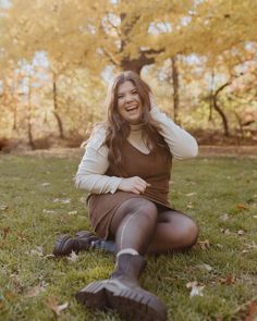 a woman sitting in the grass with her hands on her head and smiling at the camera