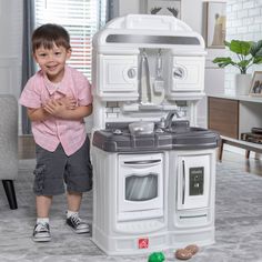 a little boy standing next to a toy kitchen