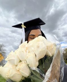 a woman wearing a graduation cap and gown holding flowers in front of her face while looking at the camera