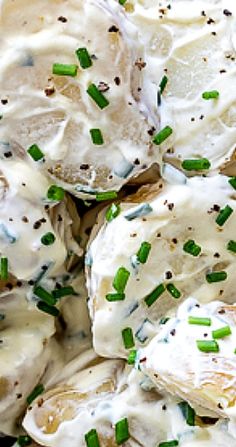 a close up view of potatoes covered in cream sauce and green onion sprinkles