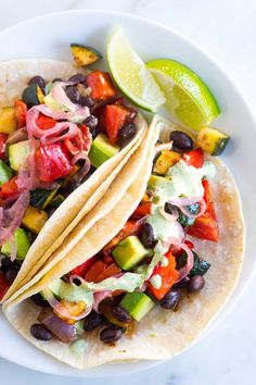 two tacos on a white plate with lime wedges