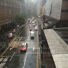 cars driving down a rain soaked street in the middle of an urban area with tall buildings