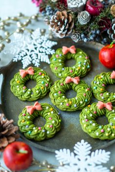 green cookies decorated with bows and sprinkles on a plate next to pine cones