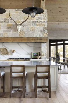 a kitchen with two stools and an island in front of a stone wall that has deer heads on it