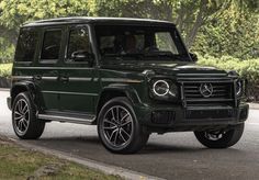 a green mercedes g - class is driving down the road