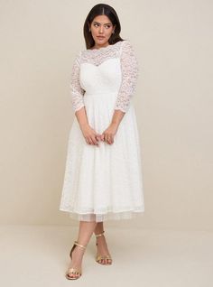 a woman is wearing a white dress with lace on the top and sleeves, standing in front of a beige background