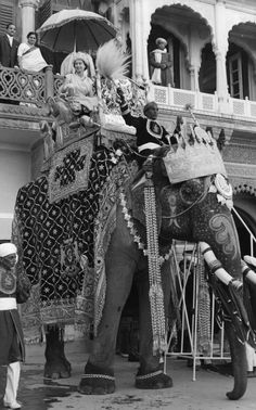 an elephant is decorated with people on it's back and some are standing in front of a building