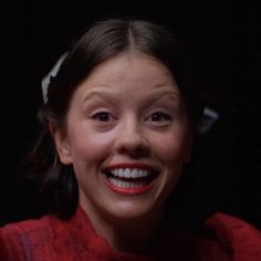 a woman smiling and wearing a red dress with white flowers on her head, in front of a black background