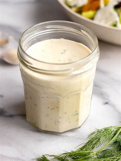 a glass jar filled with dressing next to a bowl of salad on a marble table