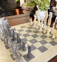 a chess board with white and black pieces on it, sitting in front of a vase filled with flowers