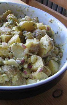 a bowl filled with potatoes and meat on top of a wooden table in front of a window