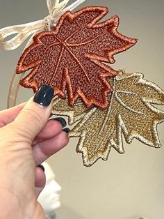 a hand holding an ornament decorated with gold and red glitter leaves on it