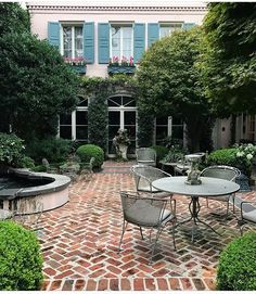 an outdoor patio with tables and chairs in front of a large white building surrounded by greenery