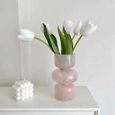 white flowers in a pink vase sitting on top of a dresser