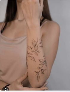 a woman is holding her hand up to her face while she has a flower tattoo on her arm