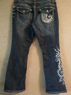 a pair of blue jeans with white embroidered designs on them hanging from a hook in front of a tan wall