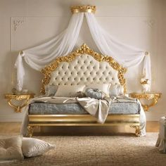 a gold and white bed in a room with pillows on the floor, curtains hanging from the ceiling