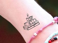 a woman's arm with a book and coffee cup tattoo on the side of it