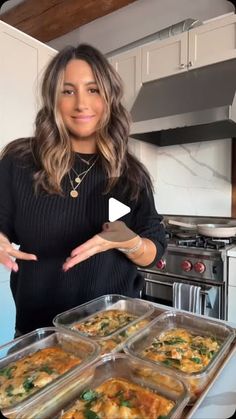 a woman standing in front of a counter filled with trays of food and holding out her hands