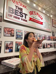 a woman is eating pizza in front of a restaurant's wall with pictures on it