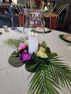 a white table topped with a vase filled with flowers and a candle next to a green leaf