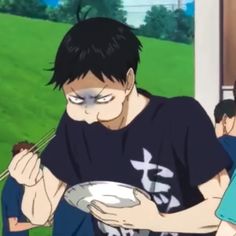 a boy holding a plate and eating food with another person standing behind him in the background